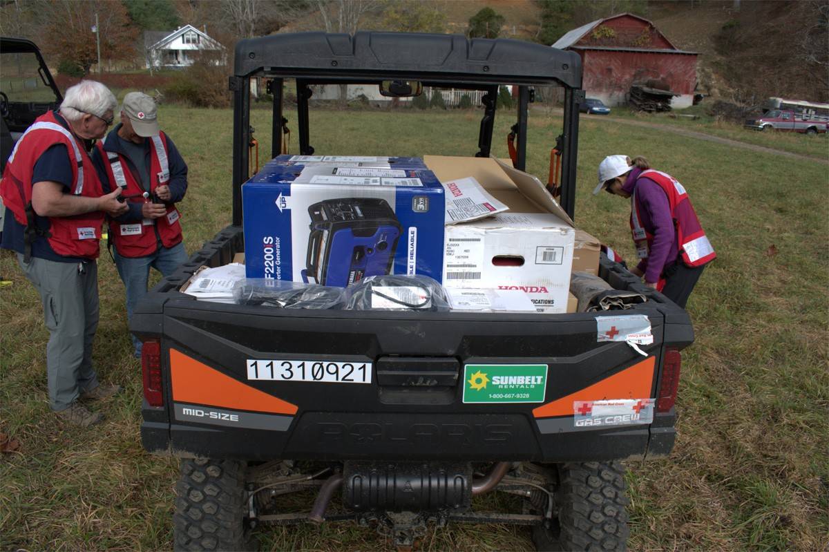 Three Red Cross volunteers are loading an all-terrain vehicle with with life sustaining supplies to help people in rural communities in Western North Carolina.